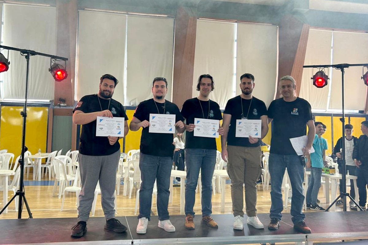 Τέσσερα μέλη της ομάδας Roboheads με μαύρες μπλούζες ομάδας στη σκηνή, κρατώντας τα διπλώματα πρώτης θέσης του RoboRAVE Greece, δίπλα σε διοργανωτή του διαγωνισμού.