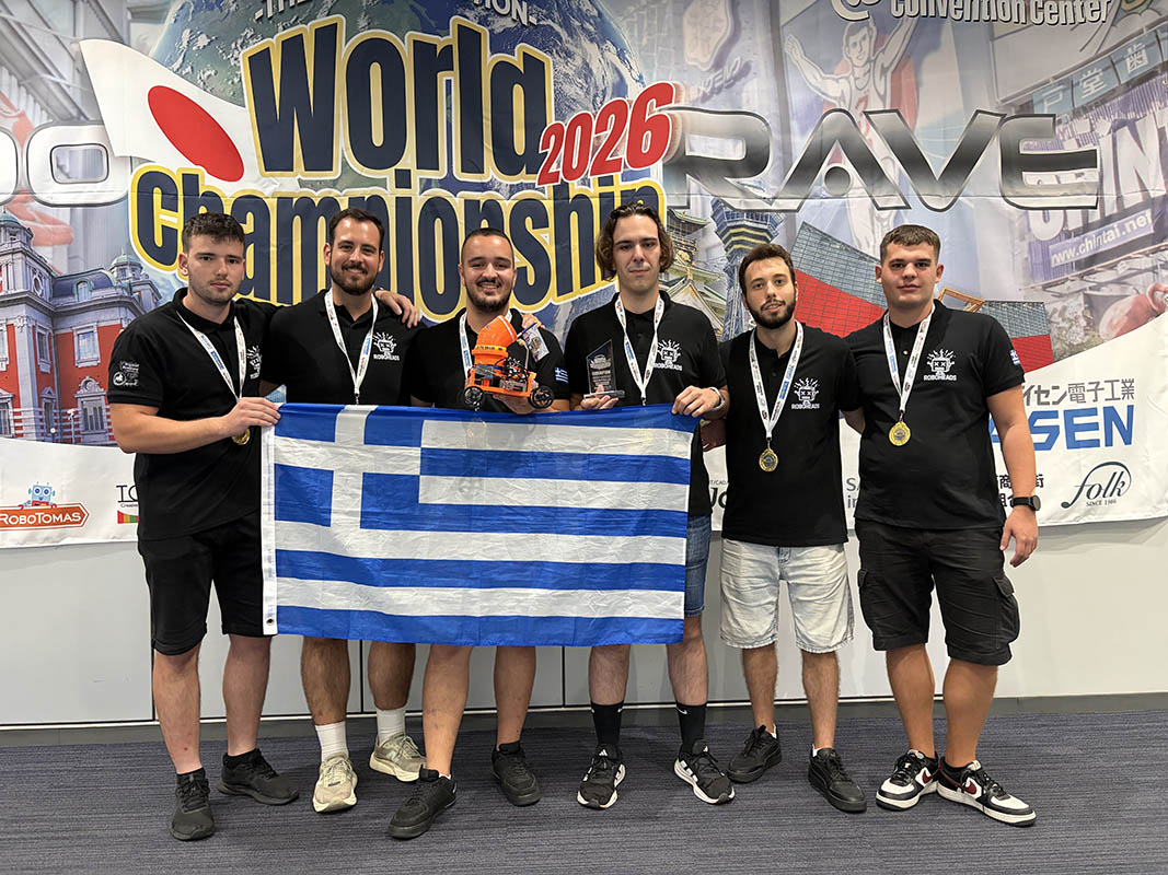 Έξι μέλη της ομάδας Roboheads με μετάλλια, κρατώντας το ρομπότ AlpineBot, ένα κύπελλο και την ελληνική σημαία μπροστά από το πανό του παγκόσμιου πρωταθλήματος.